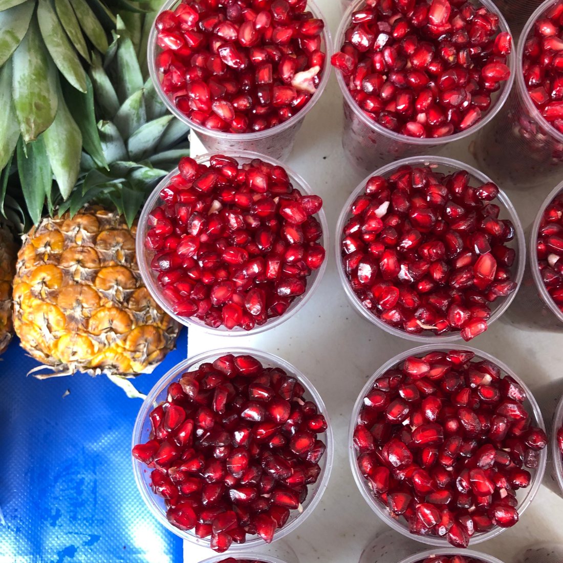 Cups of fresh pomegranate seeds beside a pineapple